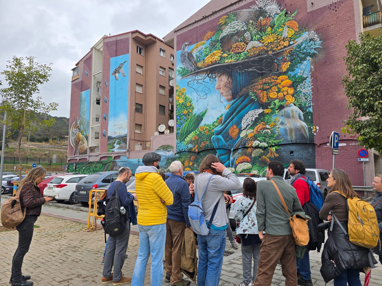 Participants of the trip seen from behind, with a mural painted on the wall of a residential building in the background.