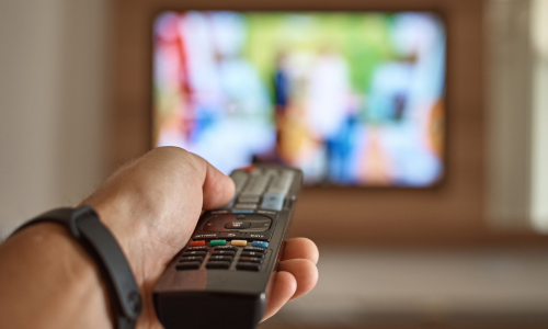 Image of a hand holding a remote control and a television in the background