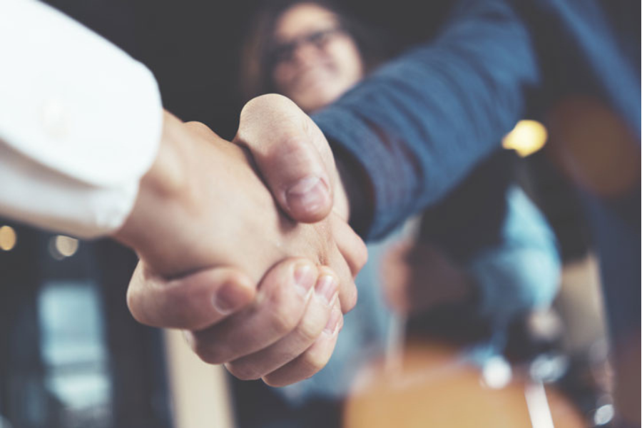 Two people shaking hands and a person in the background